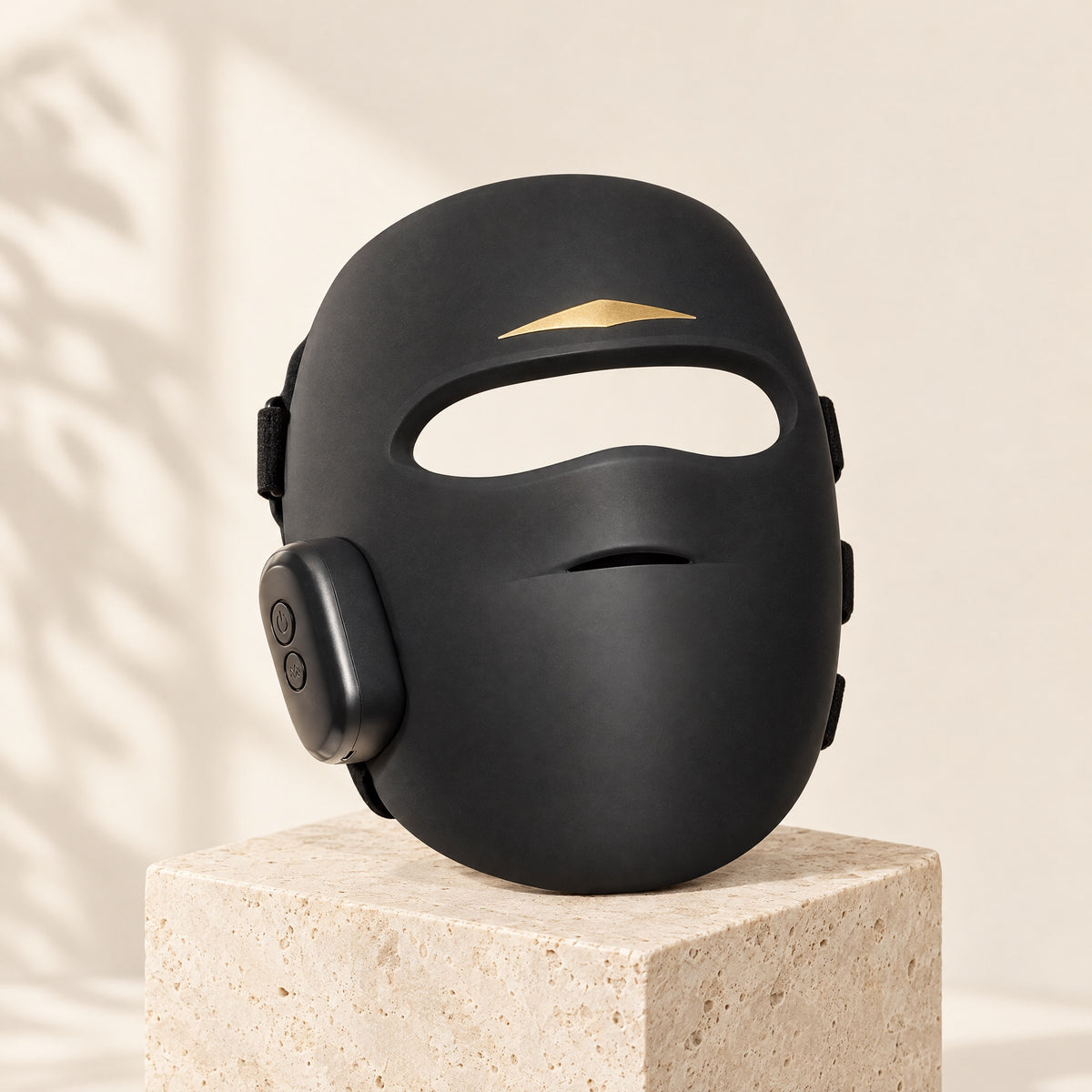 Aura Pro LED light therapy mask in black, three-quarter view on a travertine pedestal